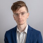 A photo of a white man with dark red hair in a blue suit and white shirt. The man is Andrew Adams, an Illinois Answers Project reporter.